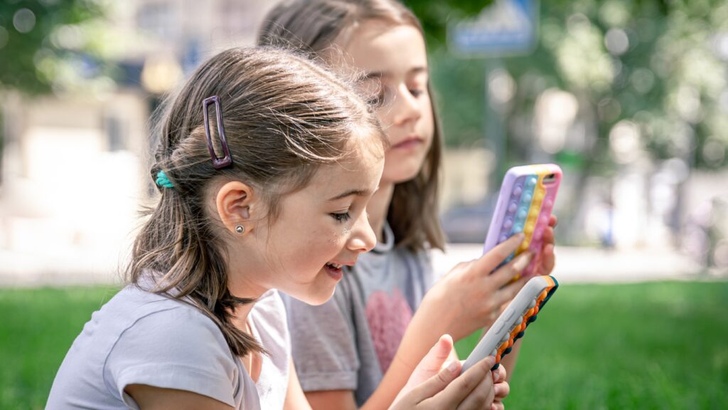 Little girls with phones sitting in apark (Freepik)