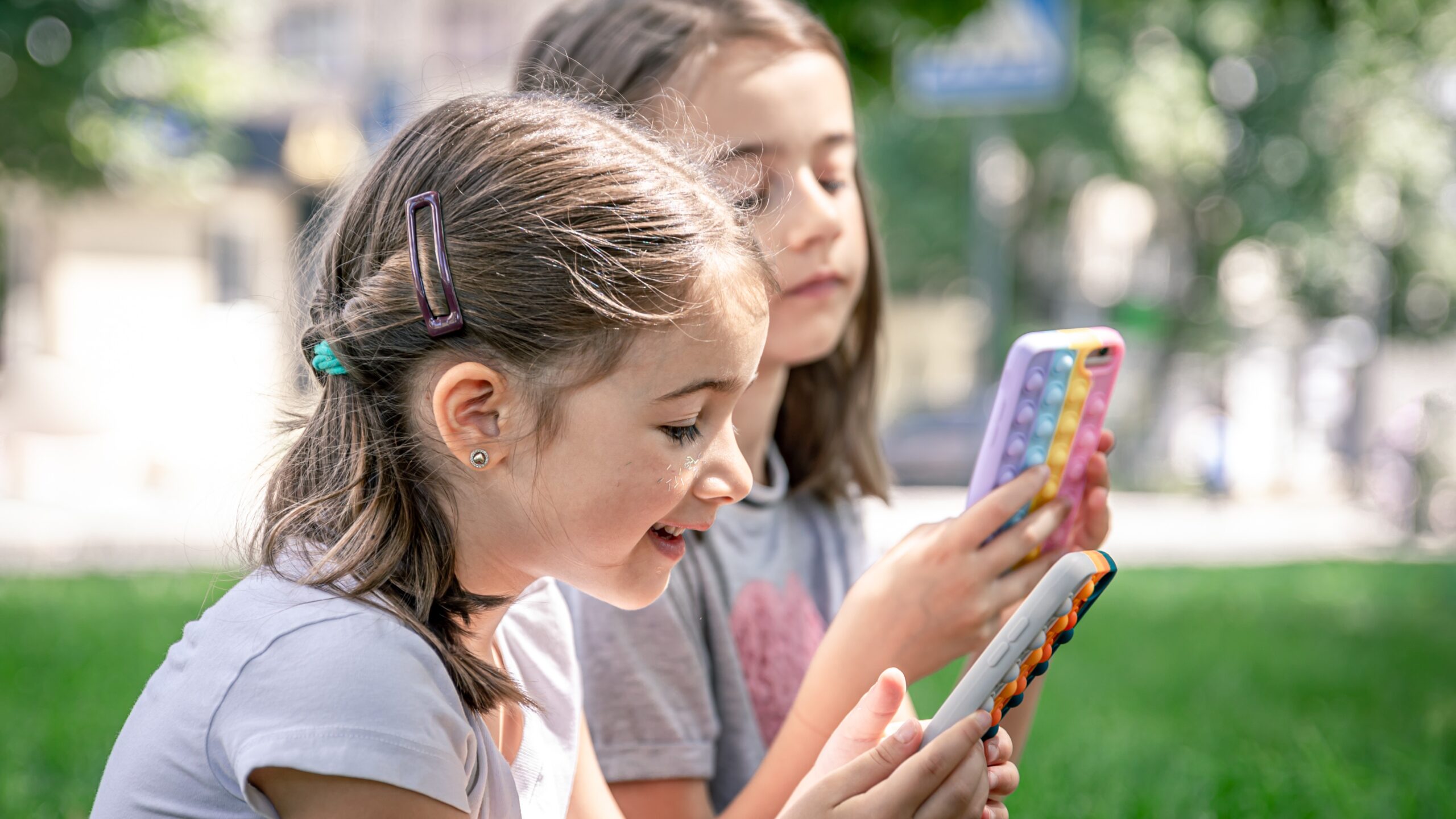 Little girls with phones sitting in apark (Freepik)