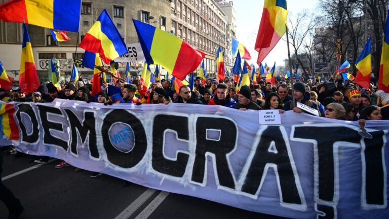 Supporters of right-wing nationalist party AUR and of presidential candidate Călin Georgescu hold a banner reading “democracy” as they march in Bucharest on January 12, 2025 to protest against the annulment of the second tour of the presidential election asking president Iohannis resign.