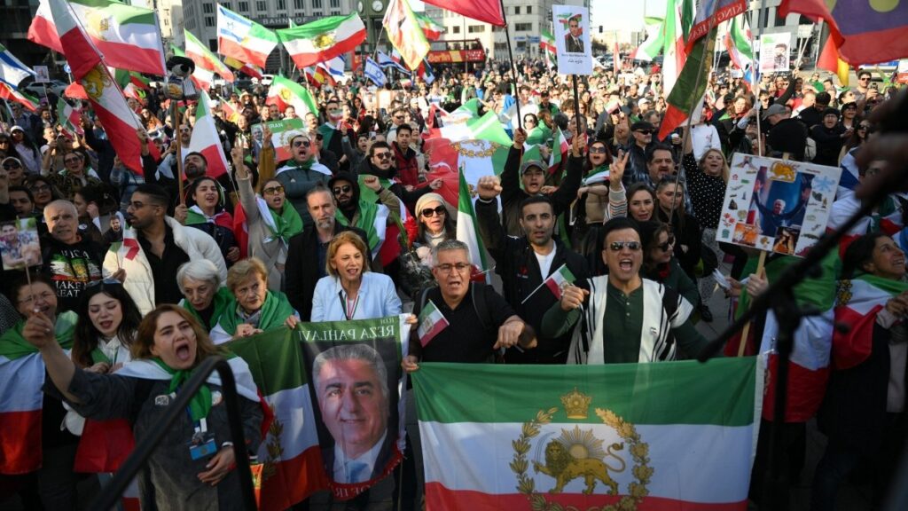 People celebrate the U.S.-Israeli strikes on the Islamic regime of Iran, holding Iranian pre-revolution Lion and Sun flags at the Potsdamer Platz in Berlin, Germany on February 28, 2026.