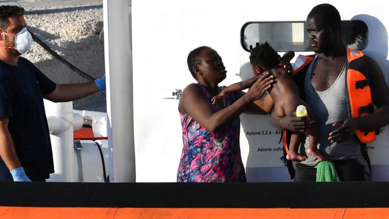 A couple with a child rescued from a migrant boat from Lybia wait to disembark from Italy's Coast Guard boat in the Italian Pelagie Island of Lampedusa on July 31, 2020.