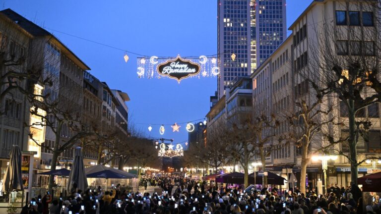 People take pictures with their mobile phones as for the first time in Germany, on March 10, 2024 in Frankfurt, a street is illuminated during the month of Ramadan.