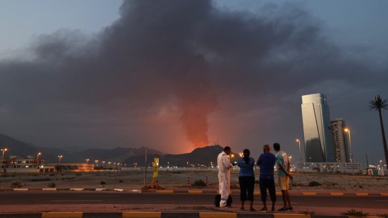 Foreign workers look at a tall plume of black smoke ascend following an explosion in the Fujairah industrial zone int he United Arab Emirates on March 3, 2026.