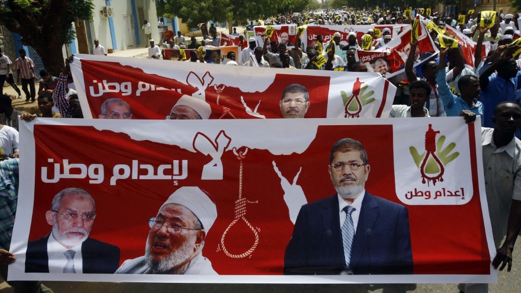 Hundreds of Sudanese Islamists hold posters bearing portraits of Egypt’s ousted president Mohamed Morsi (R), Egyptian Muslim Brotherhood leader Mohamed Badie (L) and prominent Qatar-based cleric Yusuf al-Qaradawi as they march towards a United Nations office in central Khartoum on May 22, 2015.