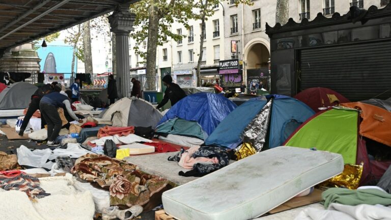 Migrants collect their belongings during the dismantling of their camp under the overhead railway line at Stalingrad metro station in Paris on November 5, 2025.