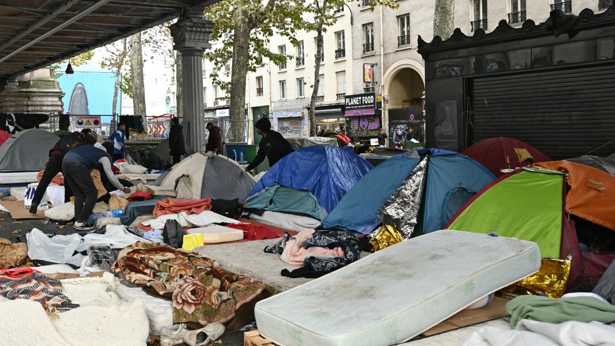 Migrants collect their belongings during the dismantling of their camp under the overhead railway line at Stalingrad metro station in Paris on November 5, 2025.