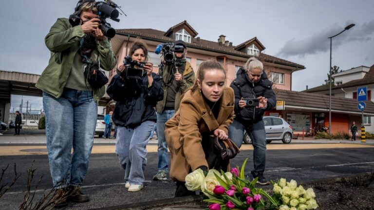 A young woman lays flowers on March 11, 2026 in Kerzers, western Switzerland where a bus caught fire on March 10, 2026, killing at least six people and injuring five others in what police said may have been a deliberate act.