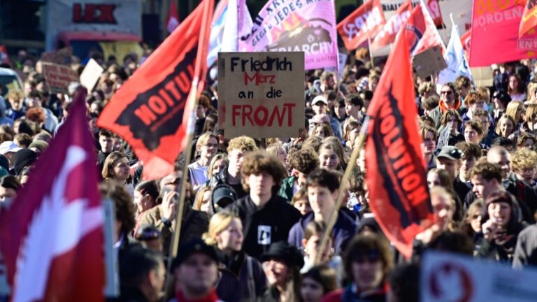 Students demonstrate with banners and a placard reading "Friedrich Merz on the front" during a protest against conscription on March 5, 2026 at Berlin's Potsdamer Platz.
