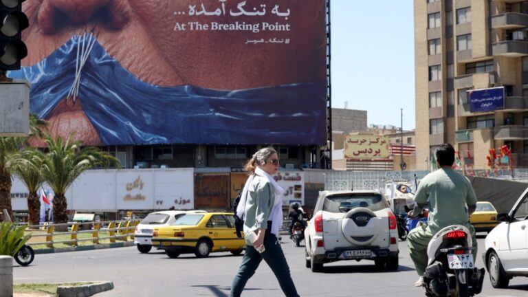 An Iranian woman walks past an anti-U.S. billboard referencing President Donald Trump and the Strait of Hormuz, installed on a building at the Valiasr Square in Tehran on May 10, 2026.