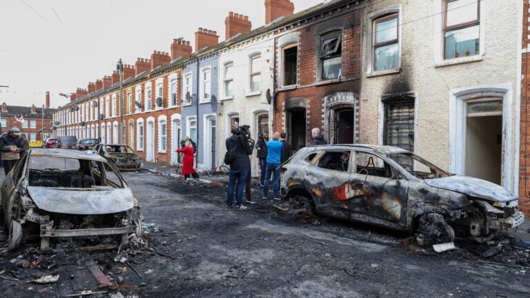 Residents and members of the media look at burnt-out cars and homes after demonstrations turned violent the night before, in eastern Belfast, Northern Ireland, on June 10, 2026.
