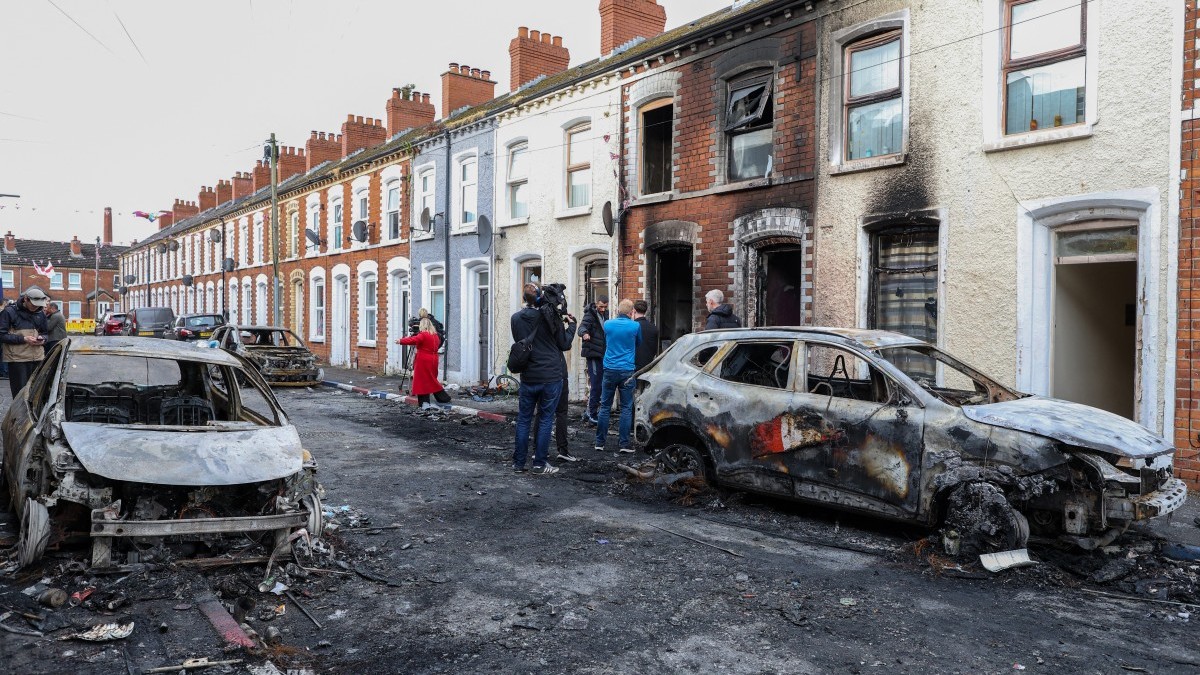 Residents and members of the media look at burnt-out cars and homes after demonstrations turned violent the night before, in eastern Belfast, Northern Ireland, on June 10, 2026.