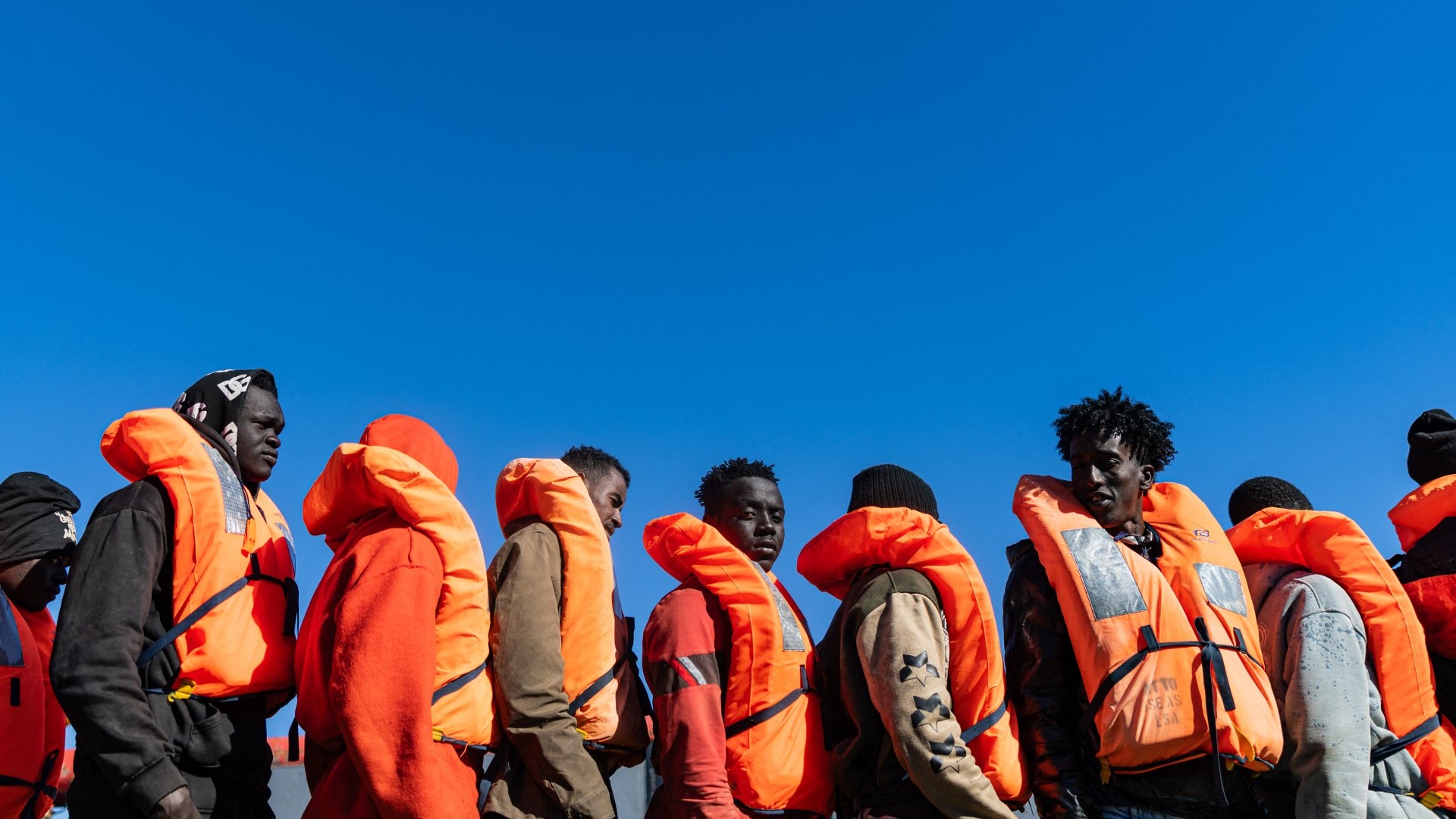 Migrants line up as they prepare to board a boat as crew members of the Ocean Viking rescue ship evacuate them from an oil tanker in the international waters between Malta and Tunisia, on December 31, 2025.