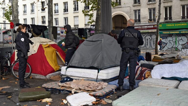 Police stand in front of migrants as they clear a camp under the overhead railway line at Stalingrad metro station in Paris early on November 5, 2025.