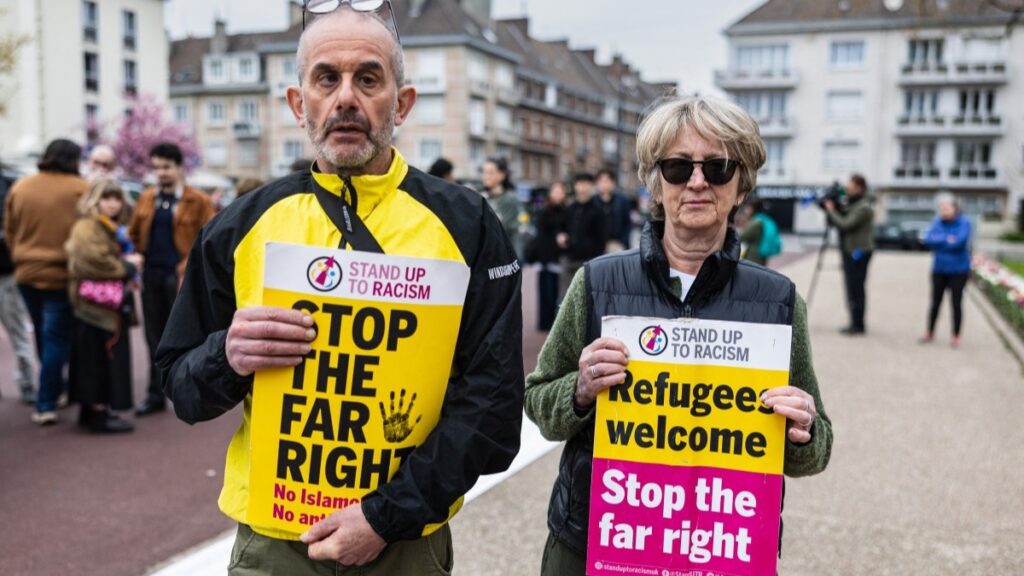 Mourners hold signs during a tribute to migrants who died crossing the English Channel in Calais, northern France, on April 10, 2026.