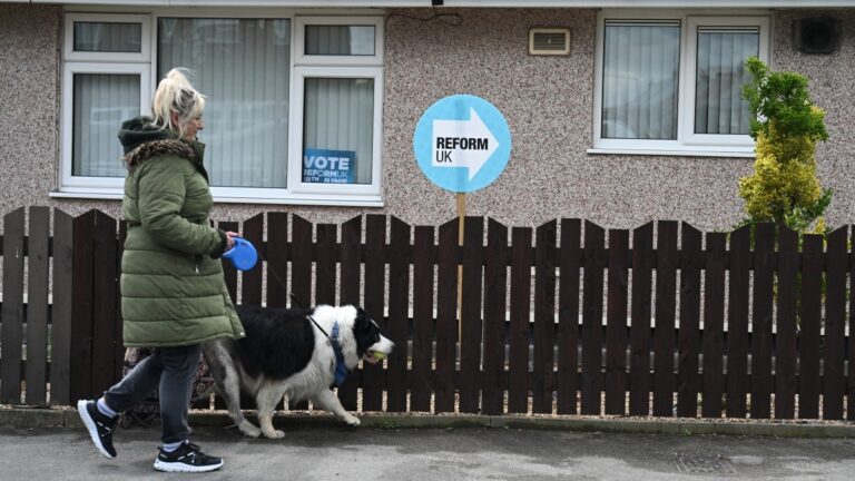 A dog-walker walks past a banner for Reform UK seen on a residential property in Bryn, west of Manchester , on June 03, 2026, ahead of the Makerfield by-election.