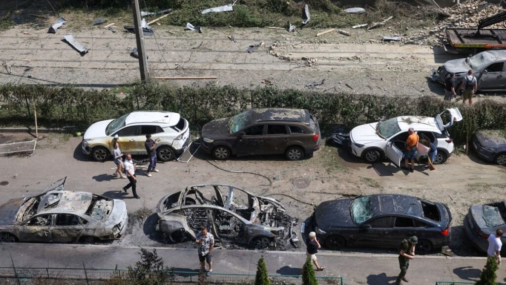 People walk past damaged cars parked in a street following missile strikes in Kyiv on July 19, 2026.