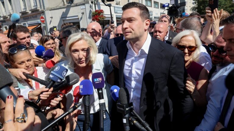 Rassemblement National (RN) party leader Marine Le Pen (C) is surrounded by journalists as she arrives with RN president Jordan Bardella (R) for a campaign gathering in the western central France city of La Fleche on July 8, 2026.
