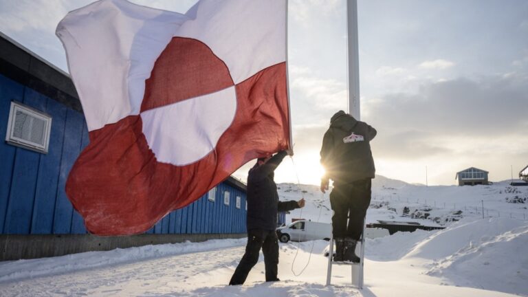 Men hoist a Greenlandic flag near polling stations, in Nuuk, Greenland, on March 24, 2026 during the parliamentary election in Denmark.