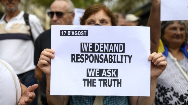 A woman holds up a sign close to where a memorial is taking place along the Las Ramblas Boulevard as the city marks the fifth anniversary of the 2017 jihadist attacks in Barcelona and Cambrils that left 16 people dead, in Barcelona on August 17, 2022.