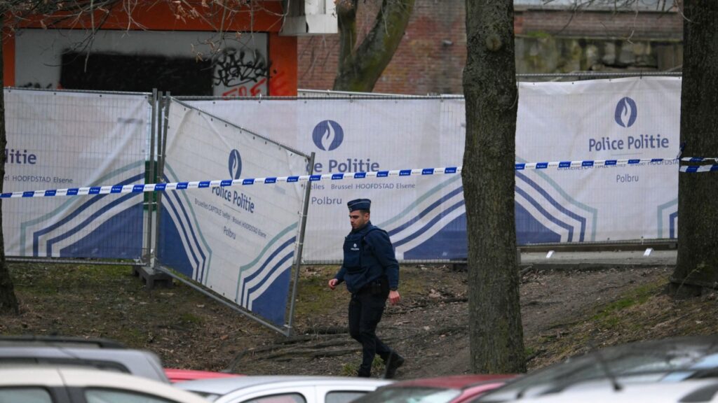 A police officer walks near a police fence blocking off an investigation area at the "Cite du Peterbos" neighbourhood, where a man was killed overnight in a new shooting linked to drug trafficking in the municipality of Anderlecht, Brussels, on February 7, 2025.