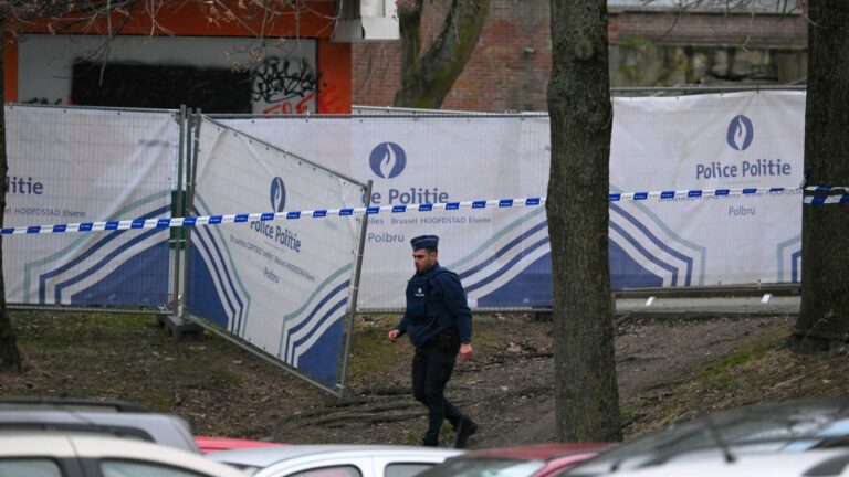 A police officer walks near a police fence blocking off an investigation area at the "Cite du Peterbos" neighbourhood, where a man was killed overnight in a new shooting linked to drug trafficking in the municipality of Anderlecht, Brussels, on February 7, 2025.