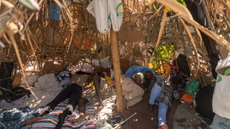 Migrants rest under a makeshift shelter as they wait to enter a short-stay migrants centre CETI at Trampolin beach in Spain’s north Africa's Ceuta enclave on August 15, 2026.