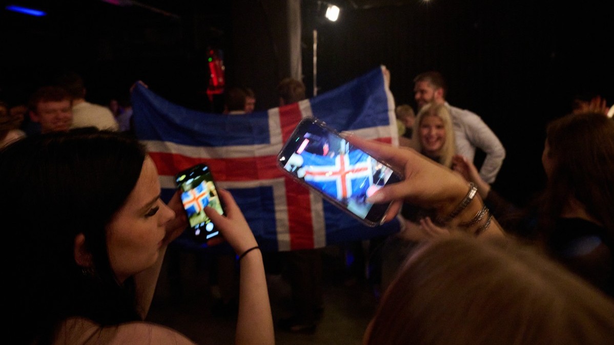 Women take pictures with their mobile phones as supporters wave an Icelandic flag during a referendum night event organised by Sfram Island, the ‘No’ campaign against resuming Iceland’s European Union accession negotiations, in Reykjavík, Iceland, on August 30, 2026.