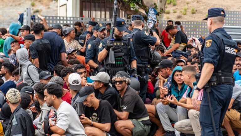 Police officers control a large group of migrants crowding outside the entrance of the Loma del Colmenar reception center, waiting for admission, in Ceuta on September 1, 2026.
